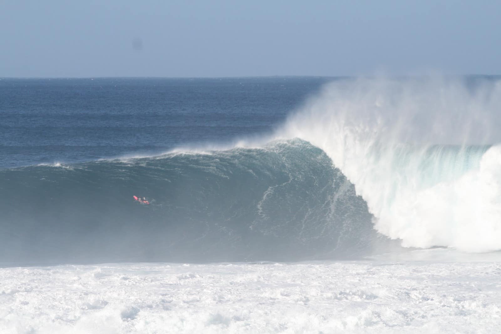 Onda a rebentar, com um surfista pequeno ao fundo.