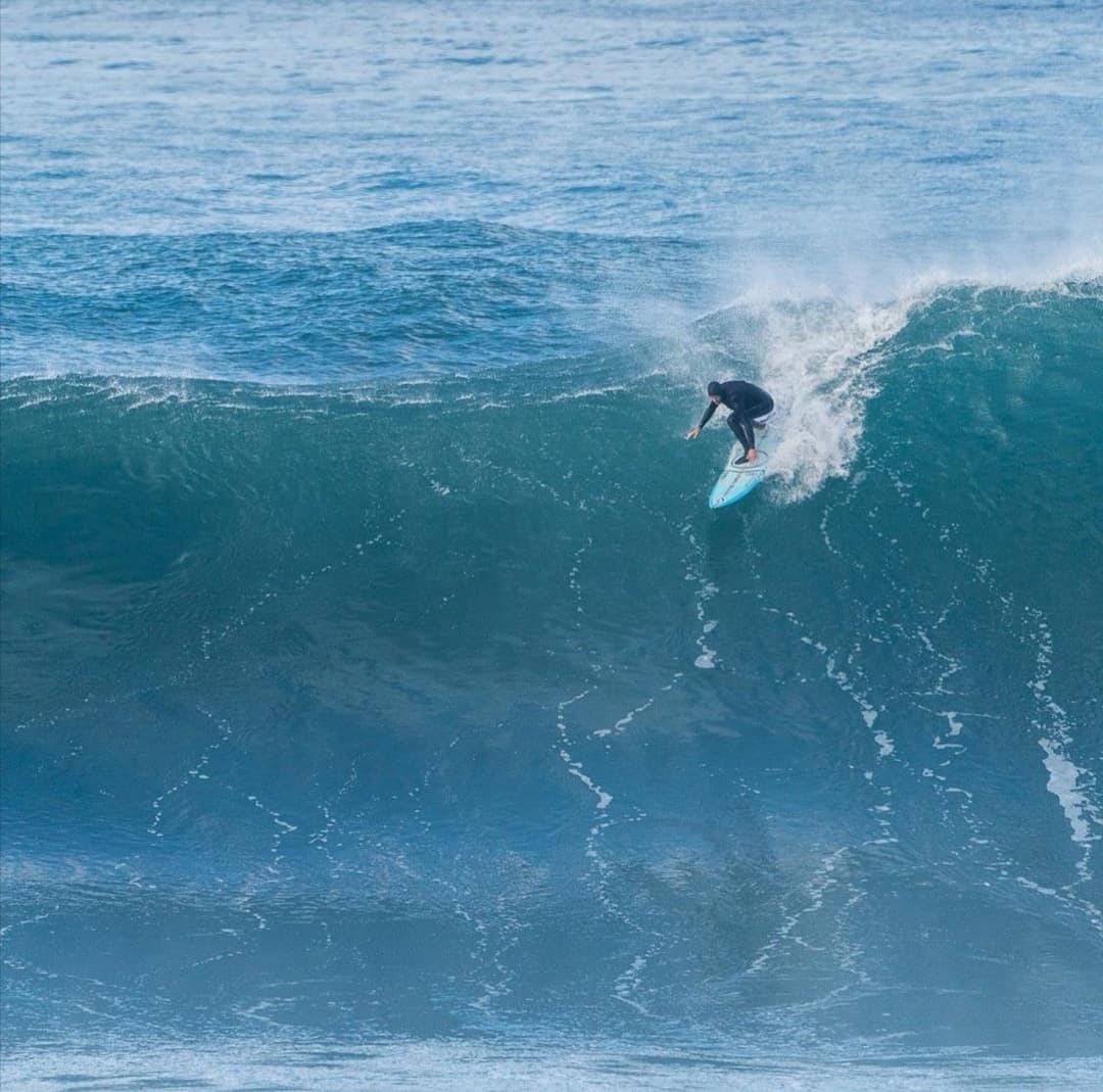 Surfista de prancha azul-clara a descer uma onda grande.